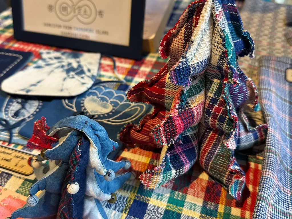 Handwoven Chongming Tubu fabric ornaments and indigo pieces displayed on the checked stall cloth.