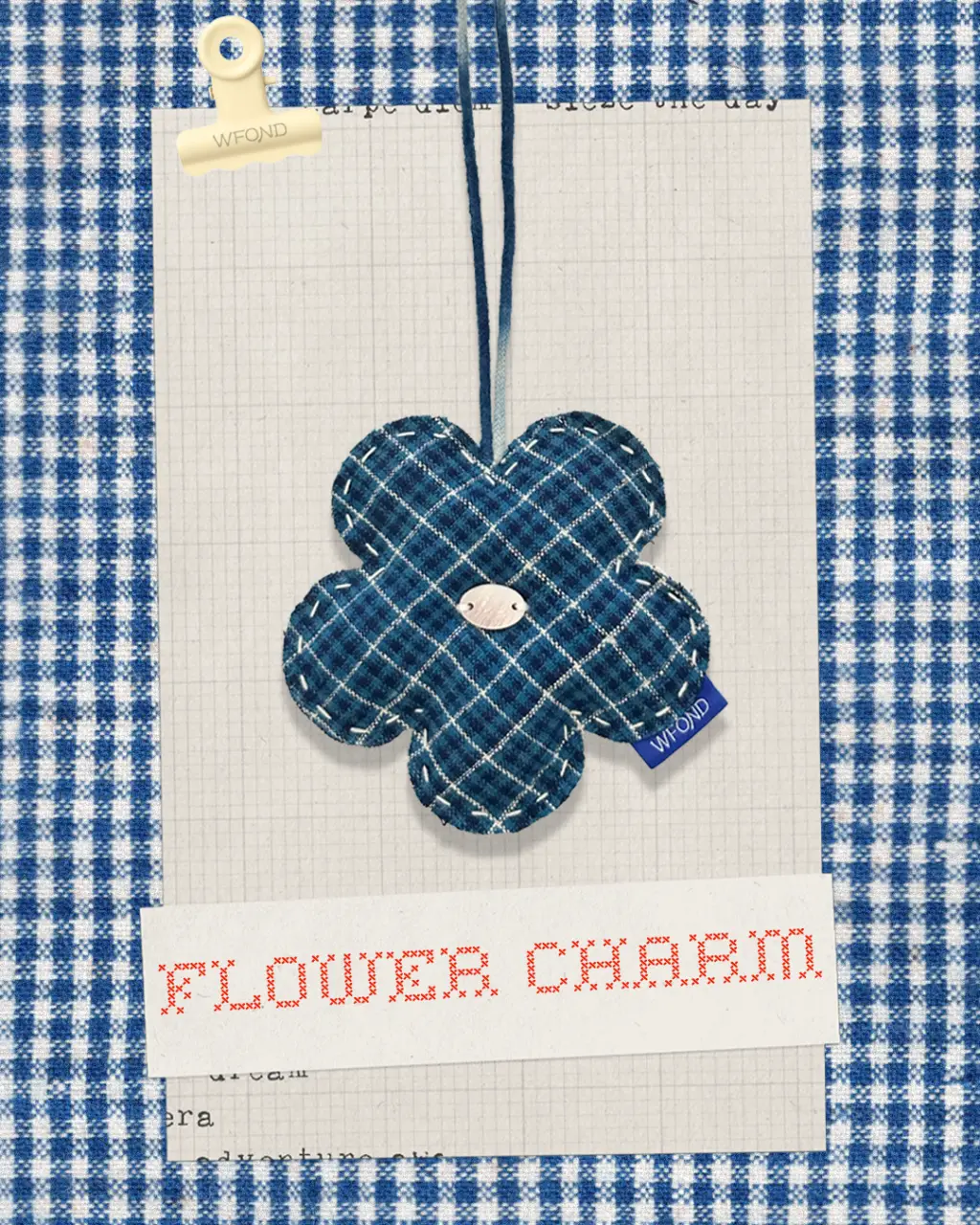 A single indigo plaid WFOND flower charm on a cord, hand-stitched with a shell-button centre, over a blue gingham background.