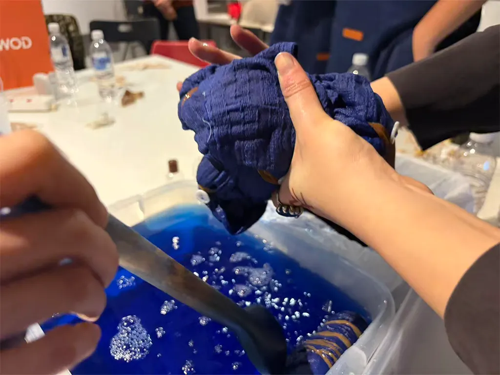 A participant lifting a bound bundle of cloth from a vat of blue indigo dye during the WFOND workshop.